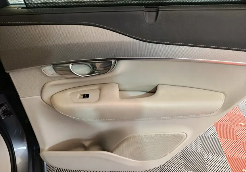 Gros plan sur la porte côté gauche beige et gris clair du Volvo XC90 T8 hybride rechargeable, avec poignée chrome et bouton vitre.
