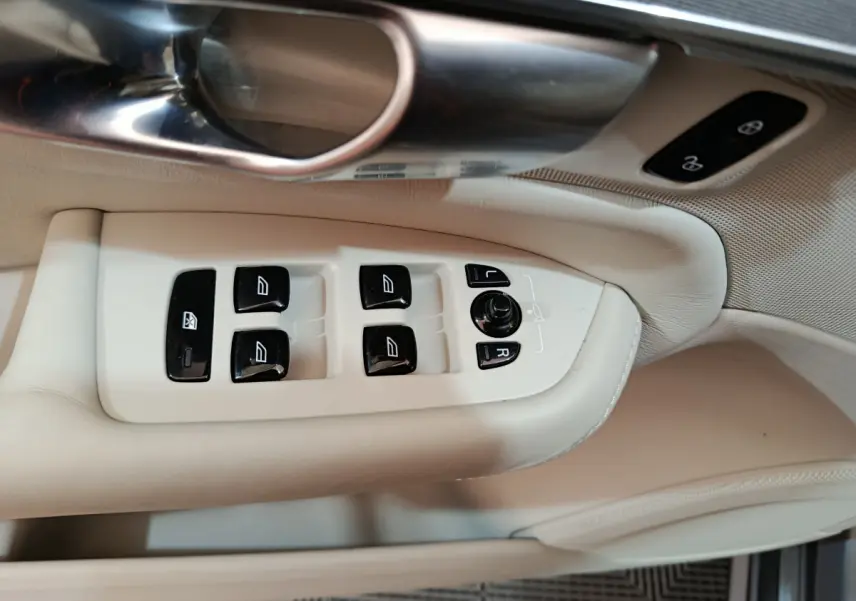 Gros plan sur les commandes de lève-vitres et rétroviseurs côté conducteur en cuir beige clair du Volvo XC90 T8 hybride.
