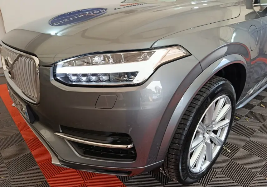 Vue 3/4 avant droit du Volvo XC90 gris clair mettant en valeur son phare LED distinctif et sa calandre verticale chromée.