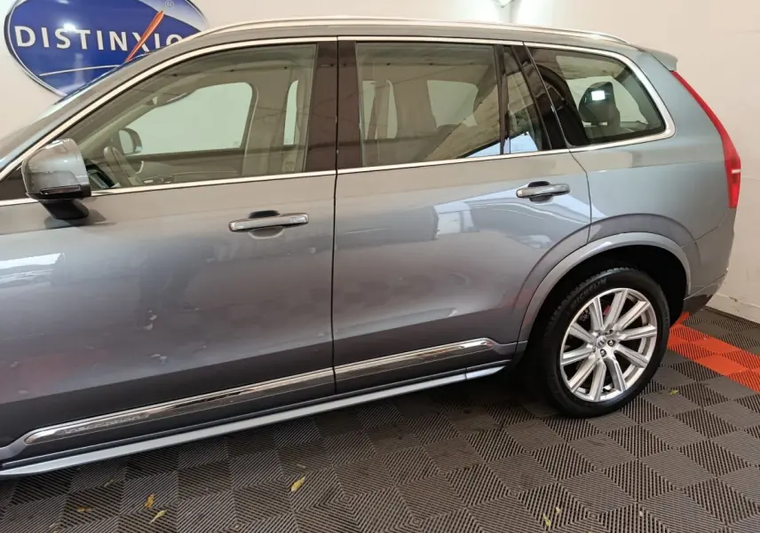 Vue latérale côté gauche d'un Volvo XC90 gris clair avec jantes alliage et vitres teintées.