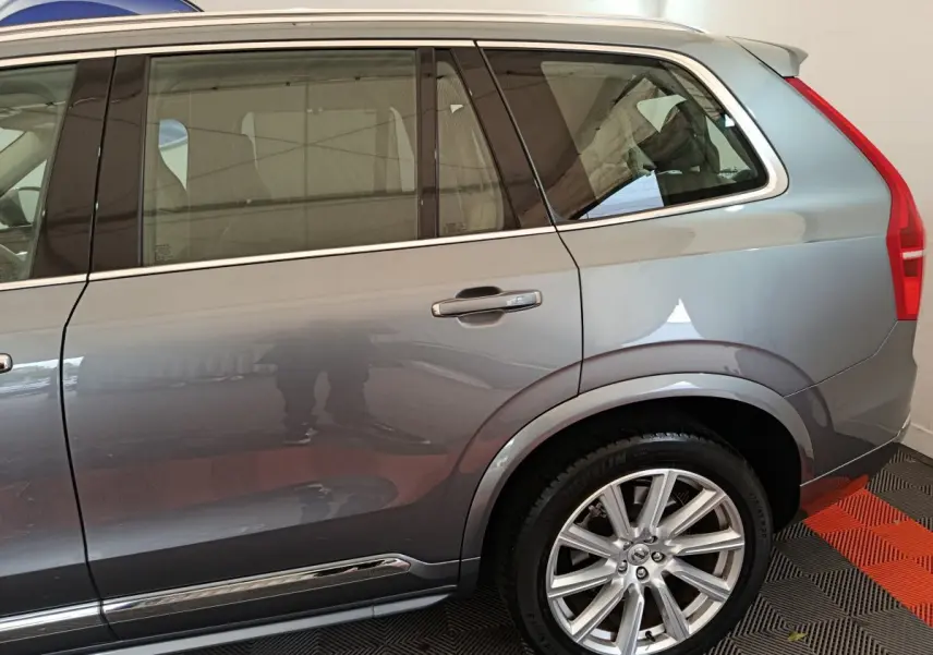 Vue côté droit arrière du Volvo XC90 T8 gris clair, mettant en valeur la roue alliage et les vitres teintées.