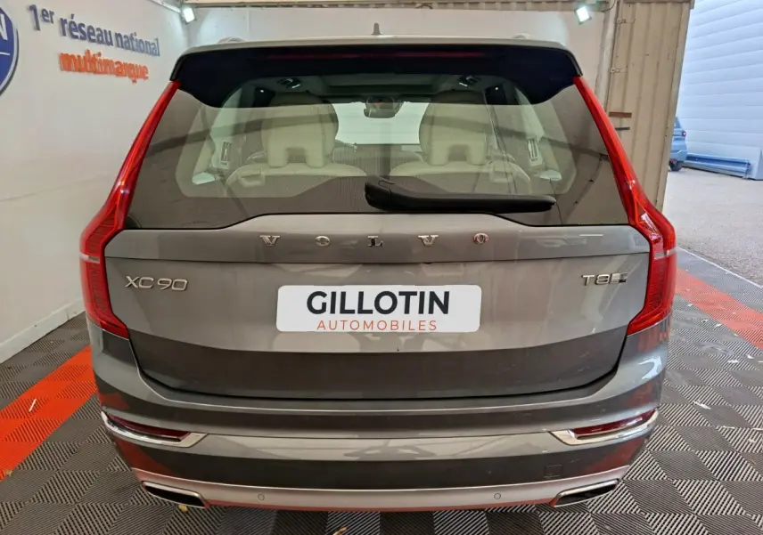 Vue arrière d'un Volvo XC90 T8 gris clair, avec feux arrière verticaux et logo visible sur coffre.