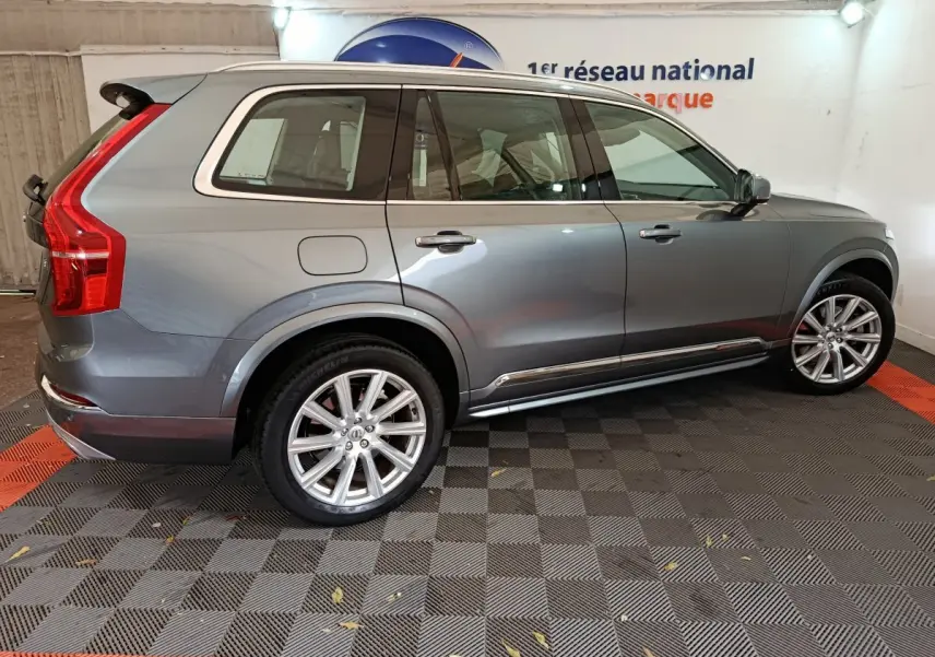 Vue de profil côté gauche d'un Volvo XC90 gris clair, mettant en valeur ses jantes alliage et ses lignes élégantes.