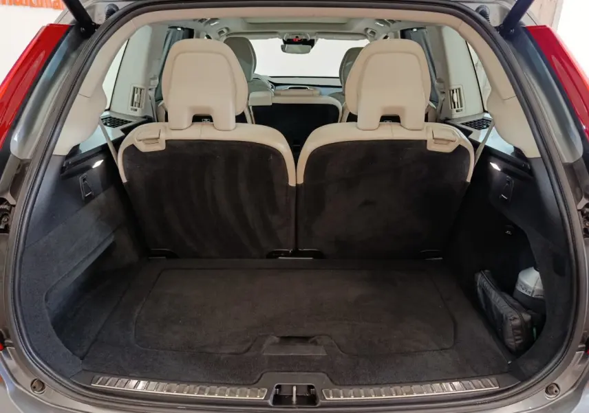 Coffre ouvert d'un Volvo XC90 gris clair, vue arrière montrant la 3ème rangée de sièges individuels beige et plancher plat.