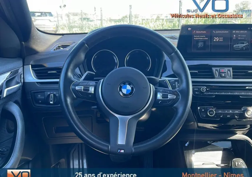 Vue intérieure centrée sur le volant cuir noir du BMW X2 F39 M35i avec tableau de bord et écran multimédia visible.
