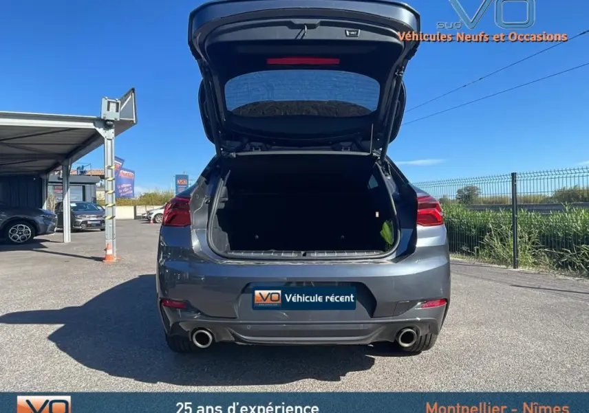 Vue arrière d'un BMW X2 gris 2019 avec coffre ouvert, double sortie d'échappement et jantes alliage 19 pouces visibles.