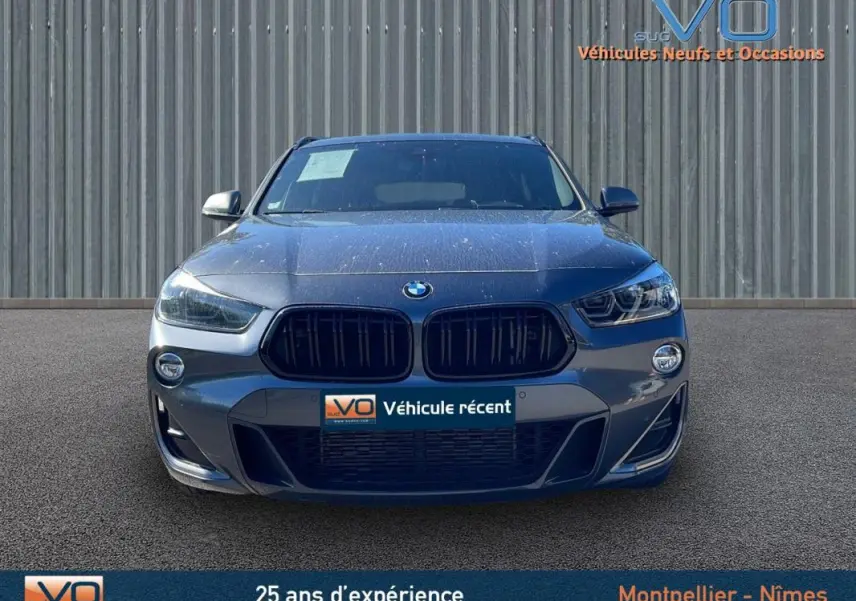 Vue frontale d'un BMW X2 F39 M35i gris 2019 avec calandre noire et phares LED allumés sur fond industriel.