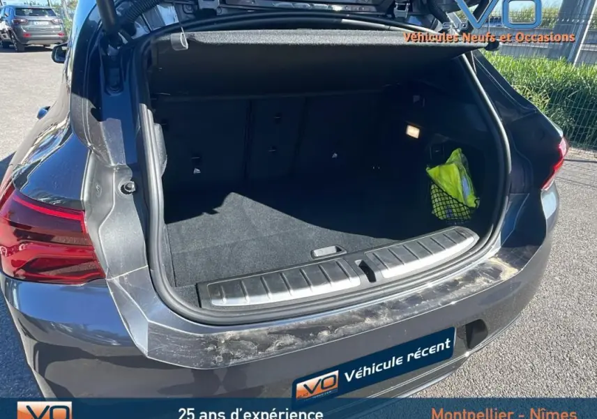 Coffre ouvert vu de l'arrière droit du BMW X2 gris 2019, montrant un intérieur spacieux et un gilet jaune dans le filet latéral.