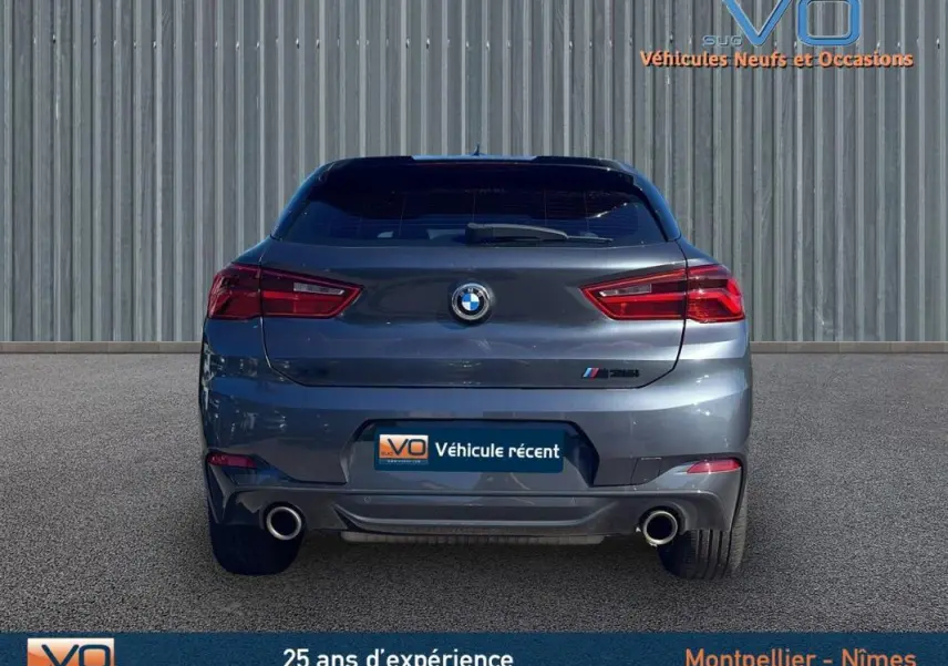 Vue arrière d'un BMW X2 F39 M35i gris avec double sortie d'échappement et feux arrière allumés.