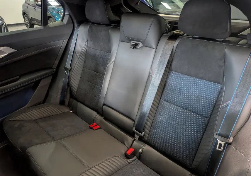 Vue intérieure sur la banquette arrière en cuir noir et alcantara avec surpiqûres rouges et ceintures de sécurité bleues.