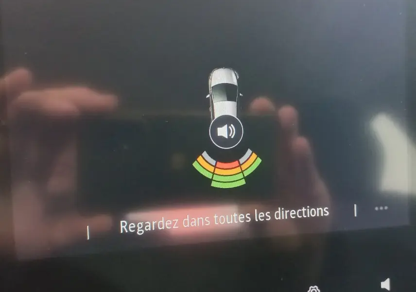 Affichage du système d’aide au stationnement avec vue aérienne d’une Renault Clio blanche, alertes de proximité colorées.