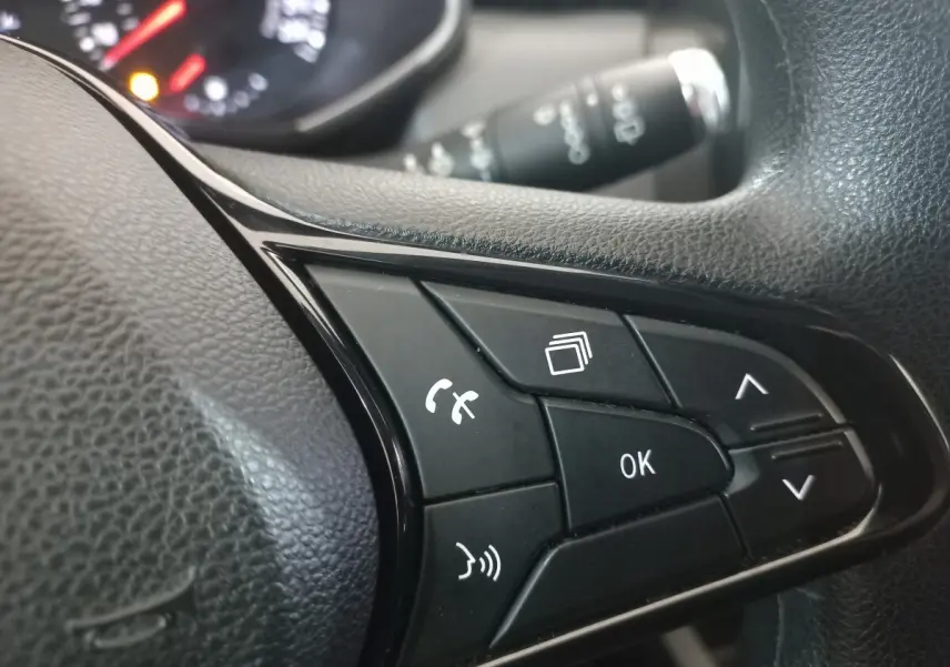 Gros plan sur les commandes noires du volant multifonctions d’une Renault Clio blanche, avec tableau de bord flou en arrière-plan.