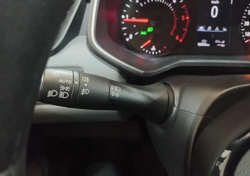 Gros plan sur la commande des phares et clignotants à gauche du volant dans une Renault Clio blanche, tableau de bord partiellement visible.