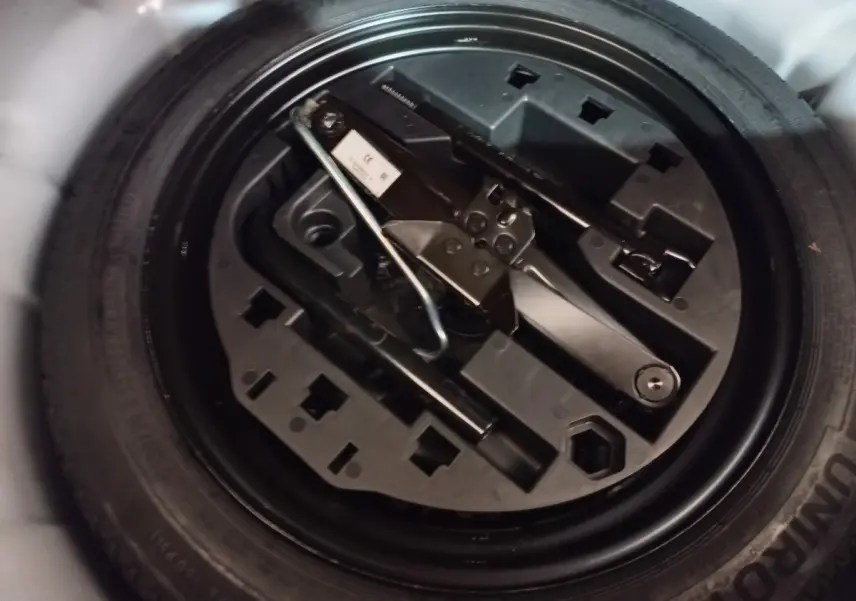 Gros plan sur la roue de secours noire et le cric rangé dans le coffre d'une Renault Clio blanche.