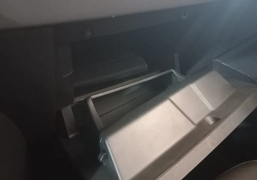 Vue rapprochée de la boîte à gants ouverte côté passager dans l’habitacle sombre d’une Renault Clio blanche.