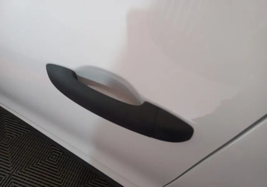 Poignée de porte noire en gros plan sur la portière blanche d'une Renault Clio Air Nav Blue dCi 85 de 2020.