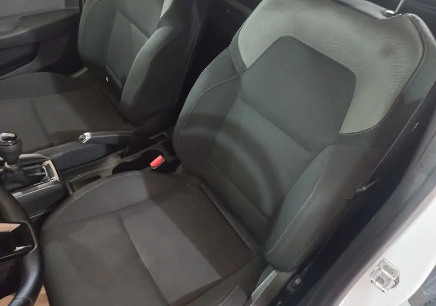 Vue intérieure côté conducteur de la Renault Clio blanche 2020, sièges tissu noir et gris, levier de vitesse manuel visible.