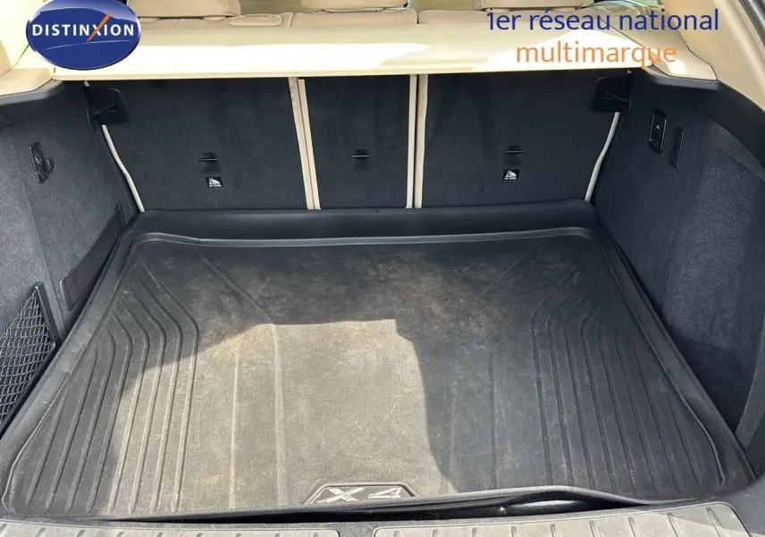 Coffre ouvert d'un BMW X4 XDRIVE 30D 2019, vue intérieure montrant le tapis de coffre noir et la garniture beige.