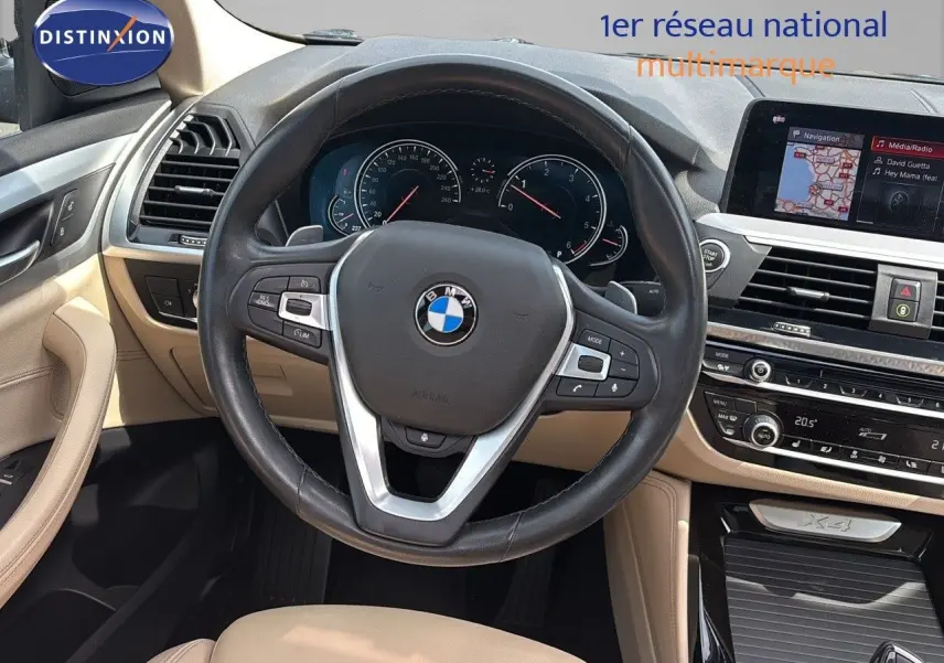 Vue intérieure du poste de conduite beige d'une BMW X4 30D 2019 avec volant cuir et écran multimédia intégré.
