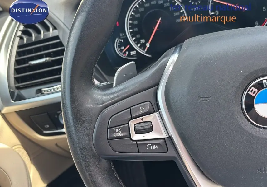 Gros plan sur le volant noir et les commandes de régulateur de vitesse du BMW X4 XDRIVE 30D intérieur beige.