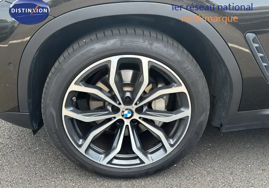 Gros plan sur la roue avant gauche d'un BMW X4 Sparkling Storm Métal avec jante alliage bicolore et logo BMW central.