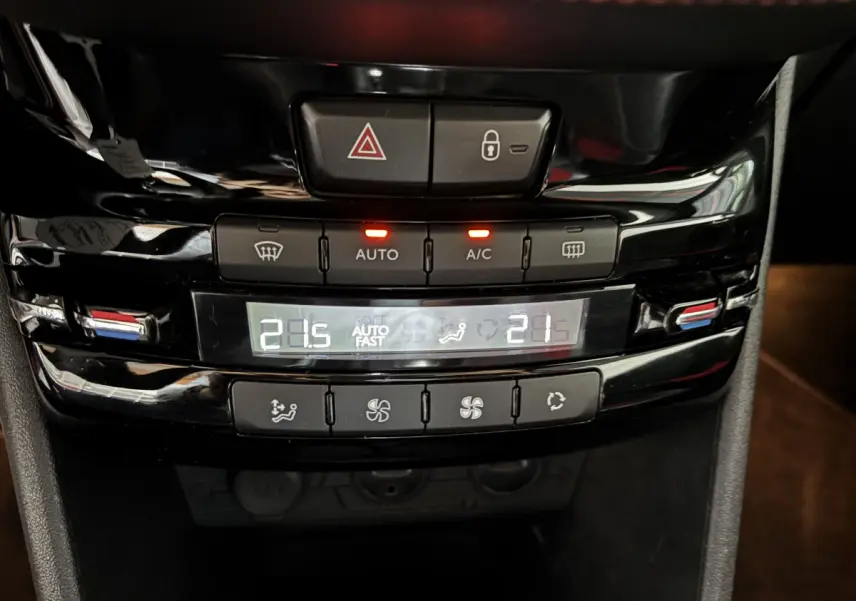 Vue rapprochée de la console centrale noire de la Peugeot 208 rouge, affichant la climatisation digitale bi-zone à 21,5°C.