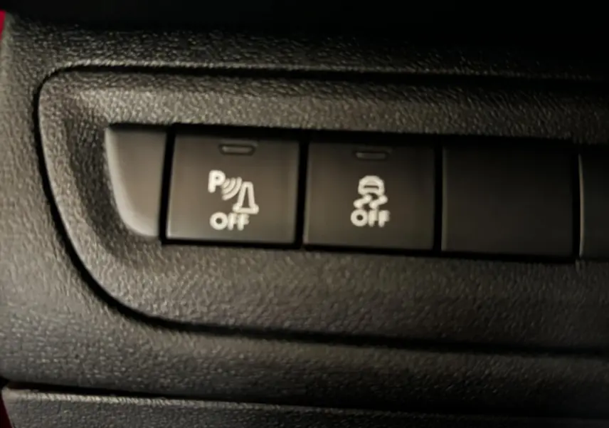 Gros plan sur les boutons de commande du système de stationnement et de l'antipatinage dans une Peugeot 208 rouge 1.6 THP 200 GTI.
