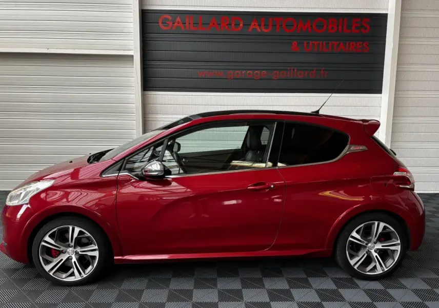 Profil côté gauche d'une Peugeot 208 GTI rouge avec jantes alliage et toit panoramique, en intérieur showroom.