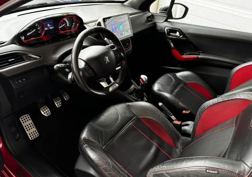 Intérieur avant de la Peugeot 208 GTI rouge, sièges cuir noir et rouge, volant GTI, tableau de bord digital et levier manuel.