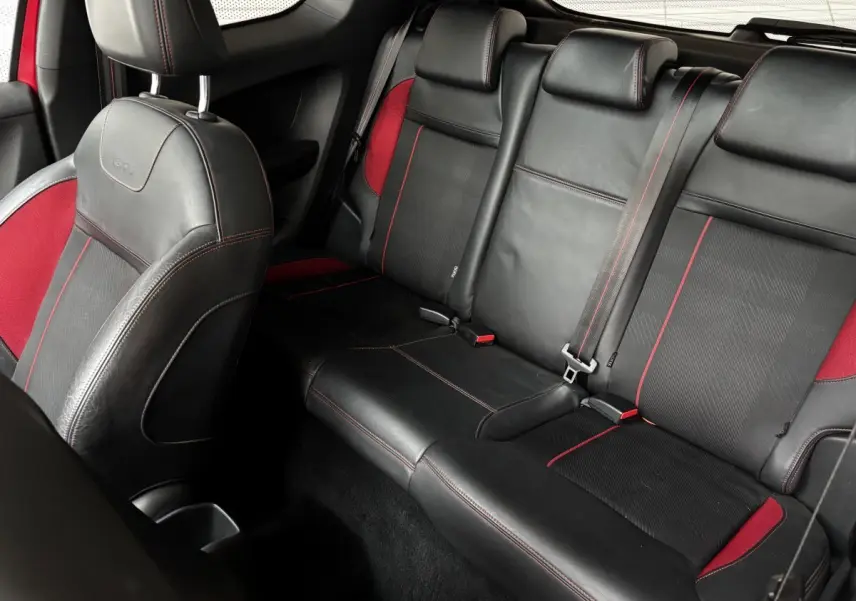 Vue intérieure arrière de la Peugeot 208 GTI 2013, sièges en cuir noir avec surpiqûres rouges et inserts rouges.