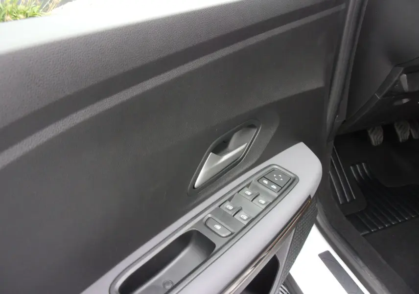 Vue rapprochée de la porte avant gauche du Dacia Jogger blanc 2025, avec commandes électriques des vitres et poignée argentée.