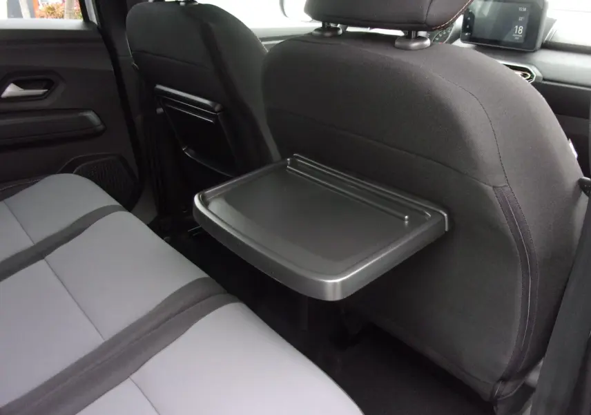 Vue intérieure arrière droite du Dacia Jogger 2025 avec tablette rabattable sur le dossier du siège avant et sièges gris.