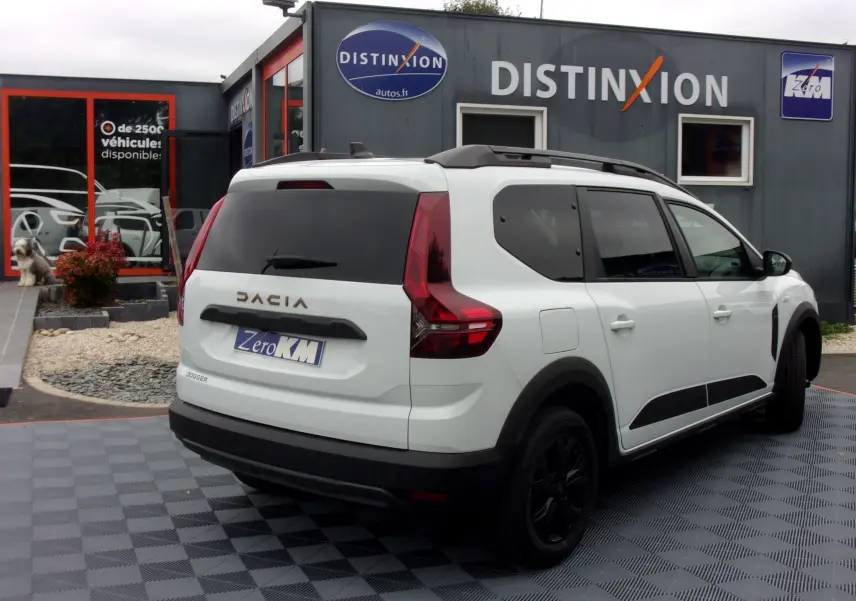 Vue 3/4 arrière droite d'un Dacia Jogger blanc 2025 avec toit noir et jantes noires devant un concessionnaire Distinxion.