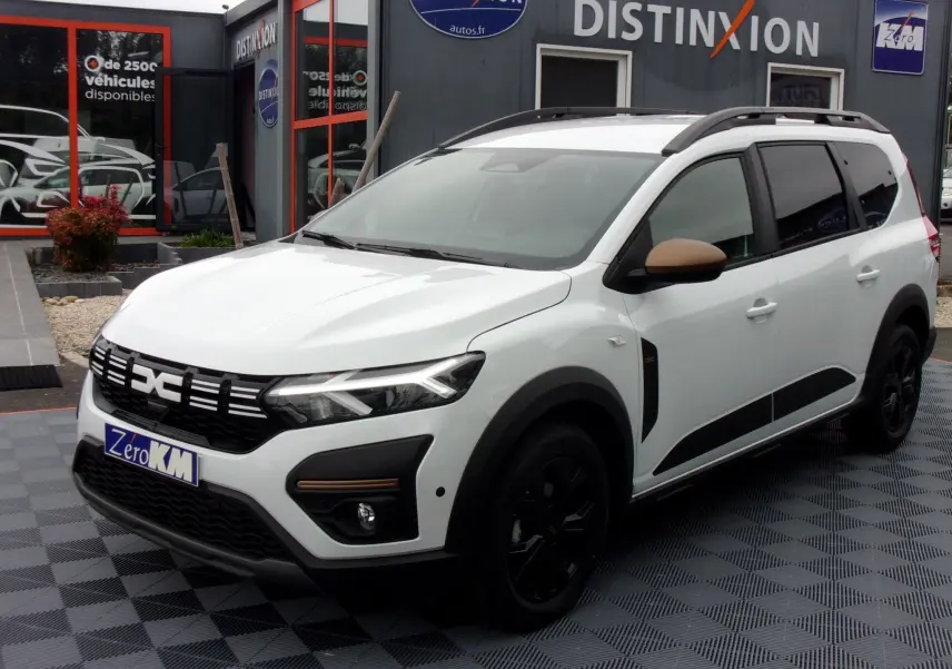Vue 3/4 avant d'un Dacia Jogger blanc avec rétroviseurs marron et jantes noires, stationné devant un concessionnaire.