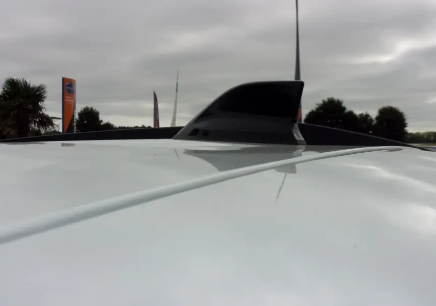 Gros plan sur l'antenne requin noire sur le toit blanc d'un Dacia Jogger 2025 sous ciel nuageux.