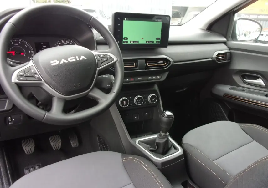 Intérieur du Dacia Jogger blanc 2025 vu côté conducteur, volant multifonction, écran tactile et boîte manuelle visible.