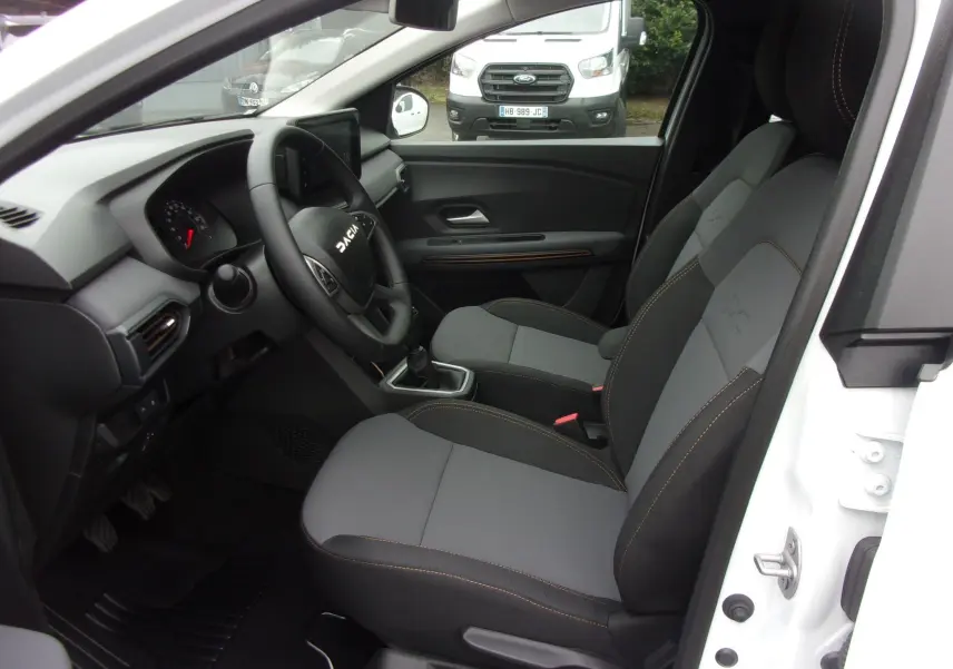 Vue intérieure côté conducteur du Dacia Jogger blanc 2025, mettant en valeur les sièges gris et la planche de bord moderne.