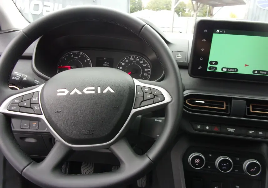Vue intérieure centrée sur le volant DACIA et le tableau de bord avec écran tactile et commandes climatiques.