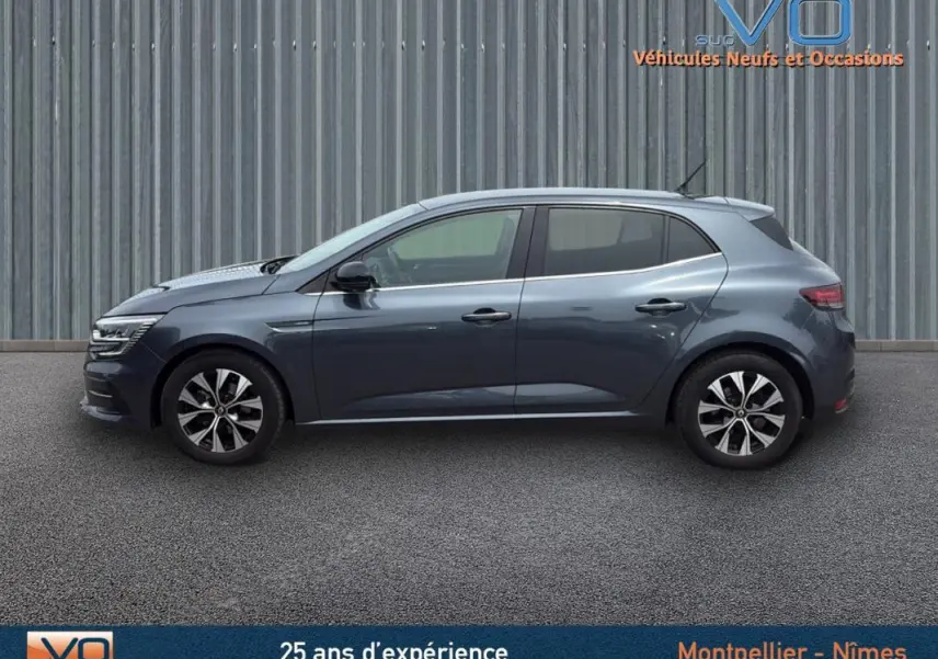 Profil latéral droit d'une Renault Mégane IV berline gris foncé avec jantes alliage 16 pouces sur fond industriel.