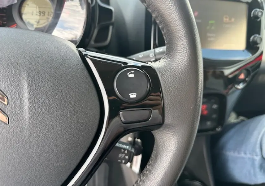 Gros plan sur le volant en croûte de cuir de la Citroën C1 rouge Scarlet avec commandes Bluetooth visibles.