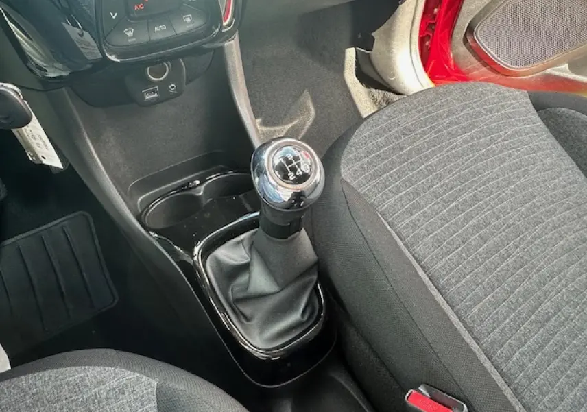 Vue intérieure centrée sur le levier de vitesses manuel et siège tissu gris de la Citroën C1 rouge scarlet 2014