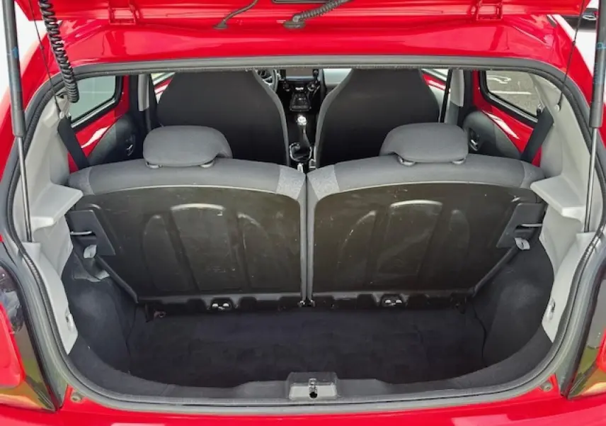Coffre ouvert vu de l'arrière d'une Citroën C1 rouge Scarlet, montrant banquette arrière et intérieur noir.