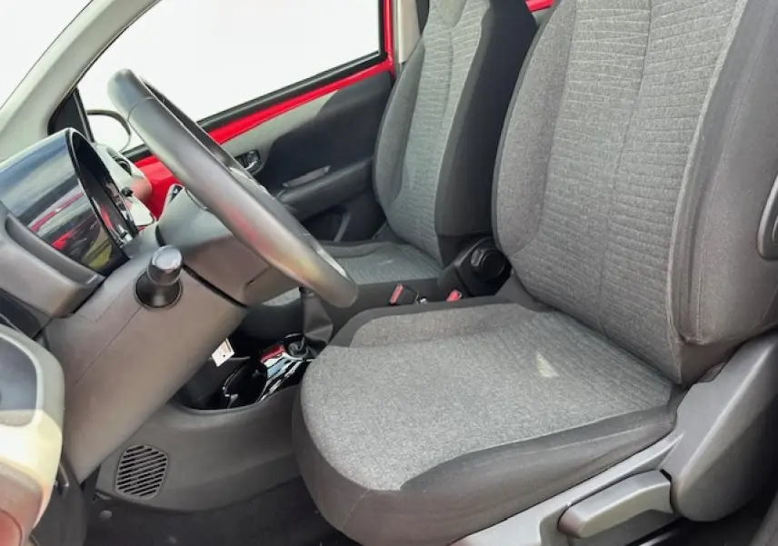 Intérieur côté conducteur de la Citroën C1 rouge Scarlet, sièges tissu gris et volant en croûte de cuir visible de profil.