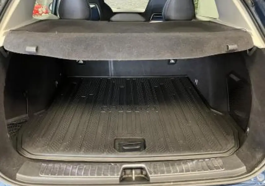 Coffre ouvert du LYNK & CO 01 bleu, vue arrière montrant la protection de coffre et la banquette arrière noire.