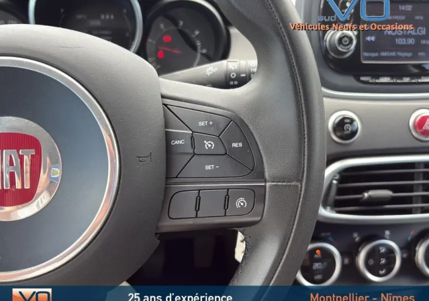 Gros plan sur le volant cuir et le tableau de bord du Fiat 500X gris anthracite avec commandes de régulateur de vitesse visibles.