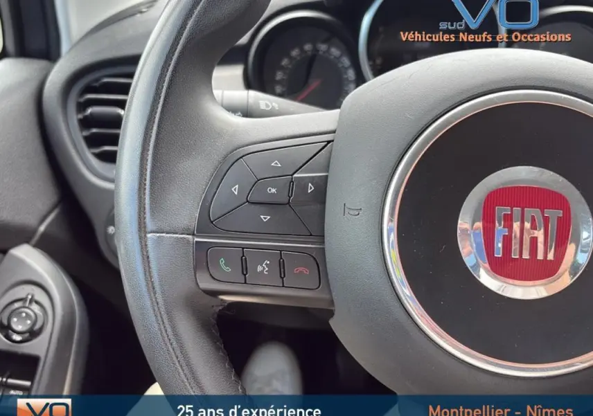 Gros plan sur le volant cuir de la Fiat 500X 2015, montrant les commandes intégrées et le logo central rouge.