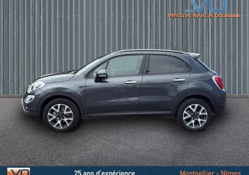 Profil côté gauche d'un FIAT 500X Cross gris anthracite avec jantes alliage 17 pouces sur fond industriel.