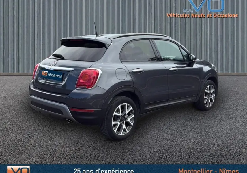 Vue 3/4 arrière droite d'une FIAT 500X Cross gris anthracite avec jantes alliage 17 pouces sur sol bitumé.