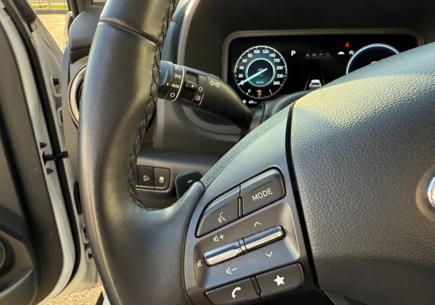 Gros plan sur le volant noir et le tableau de bord numérique du Hyundai Kona blanc Atlas, côté gauche, intérieur éclairé.