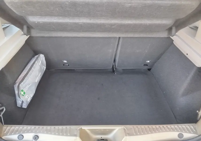 Coffre ouvert d'une Dacia Sandero Stepway beige dune 2020, montrant un espace de chargement propre avec une trousse de sécurité grise sur le côté gauche.